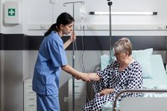 an older woman in a hospital bed with a nurse holding the hand of her patient