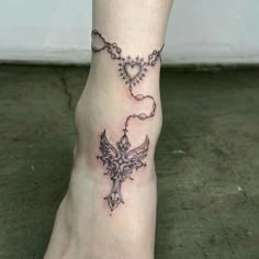 a tattoo on the foot of a woman with a cross and heart shaped beads hanging from it