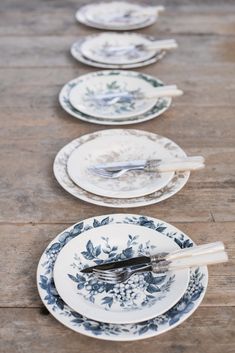 several plates with spoons and forks lined up on a wooden table in front of each other