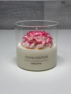 a candle with pink flowers in it on a white countertop next to a wooden wall