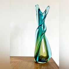 a green and blue vase sitting on top of a wooden table next to a white wall