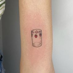 a small strawberry in a glass tattoo on the arm