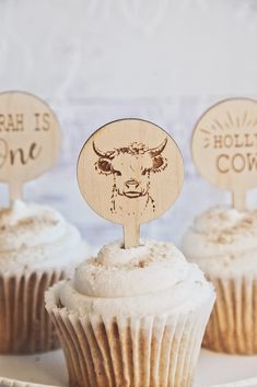 three cupcakes on a white plate with wooden picks in the shape of cows