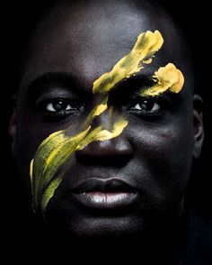 a man with yellow paint on his face and black skin is looking at the camera