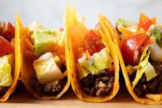 three tacos with meat, lettuce and tomatoes on them are lined up