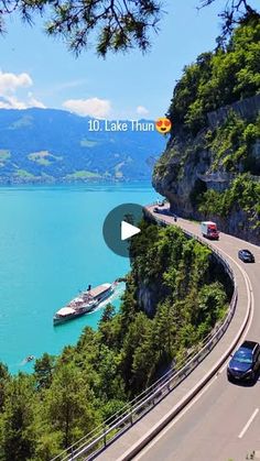 cars are driving down the road next to a large body of water with boats on it