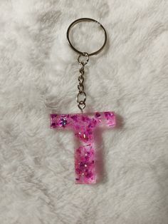 the letter t is made out of pink glitter and has a keychain attached to it