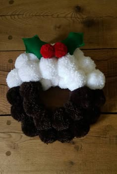 a christmas wreath made out of wool and felt with holly leaves on top, sitting on a wooden surface