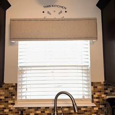 a kitchen sink under a window with roman shades on the windowsill and tile backsplash