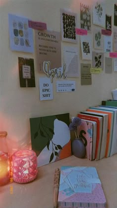 a desk with many books on it next to a lit candle and some pictures hanging on the wall