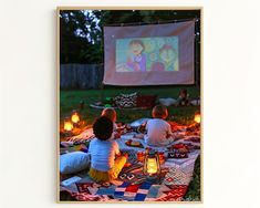 three people sitting on a blanket in front of a movie screen with candles lit up