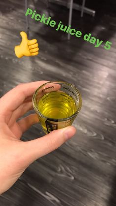 a hand holding a small glass filled with green liquid next to a sign that says pickle juice day 5