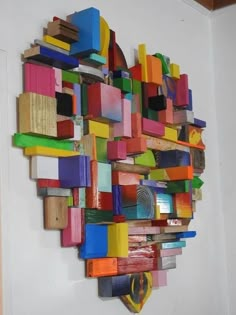 a sculpture made out of different colored objects on a white wall next to a chair