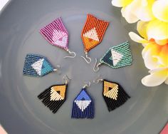 four pairs of beaded earrings sitting on top of a plate next to a flower