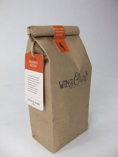 a brown paper bag with an orange tag on the front and side of it that says wing & thread