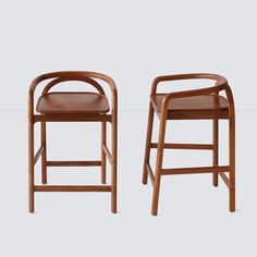 two wooden chairs sitting next to each other on a white surface with one chair facing the camera