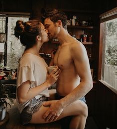 a man and woman kissing in the kitchen while sitting on top of a counter next to each other