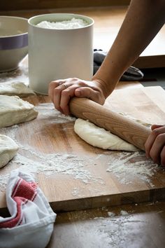 a person kneading dough on top of a wooden cutting board