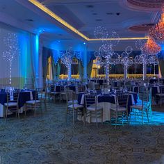 a banquet room set up with blue and white linens, chandeliers and tables