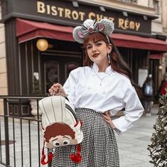 a woman is standing on the sidewalk with her hand in her pocket and wearing a mouse ears hat