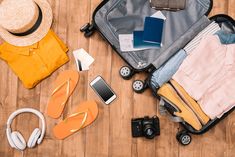 an open suitcase sitting on top of a wooden floor next to shoes and headphones