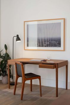 a wooden desk with a lamp on it in front of a painting and potted plant