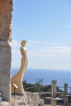 the statue is standing next to an old building with a view of the ocean in the background