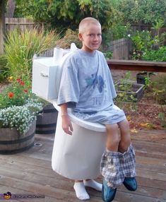 a young boy sitting on top of a toilet in a backyard with his feet up