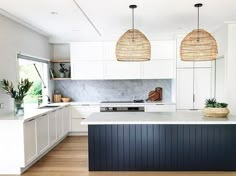 an island in the middle of a kitchen with two pendant lights hanging over it's head