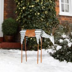 a metal bird sculpture sitting on top of snow covered ground next to a brick building