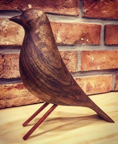 a wooden bird sitting on top of a wooden table next to a brick wall in the background