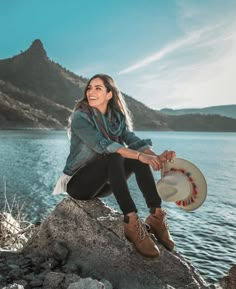 a woman sitting on top of a rock near the water