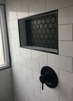 a black and white bathroom with hexagonal tiles on the wall, toilet paper dispenser and window