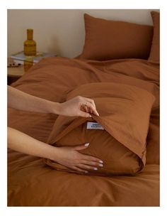 a person reaching for a pillow on top of a bed with brown sheets and pillows