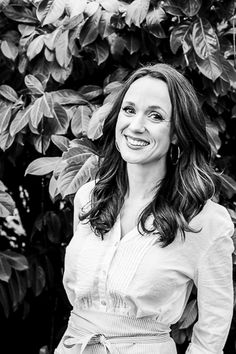 a black and white photo of a smiling woman in front of some trees with leaves