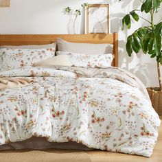 a bed with white and pink flowers on it in a room next to a potted plant