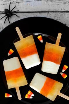 four popsicles with candy corn on them sitting in a black plate next to a spider