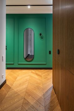 an empty room with green walls and wooden floors, mirror on the wall in the corner