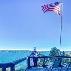 a woman standing on top of a wooden deck next to an american flag flying in the wind