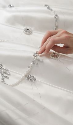 a woman's hand on a white dress with beads and chains attached to it