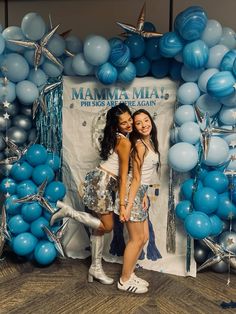 two young women posing in front of a backdrop with balloons and streamers for the mamma mia photo booth