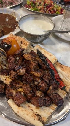 an assortment of meats and vegetables on a silver platter with other dishes in the background