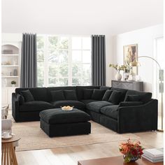 a living room with a large sectional couch and ottoman in front of a window that has curtains