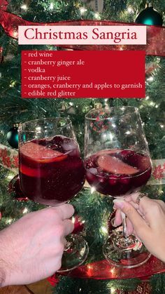 two people toasting glasses of red wine in front of a christmas tree with the words christmas sangria on it