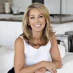 a woman sitting on a white couch in a kitchen smiling at the camera with her legs crossed