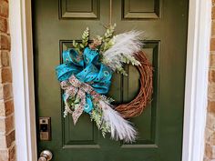 a green door with a wreath and feathers hanging on it's front door handle