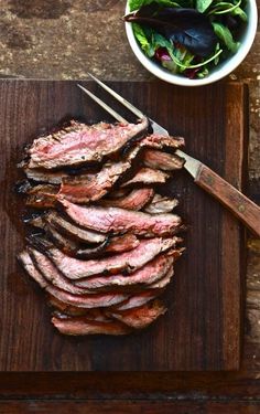 sliced steak on a cutting board next to a bowl of salad