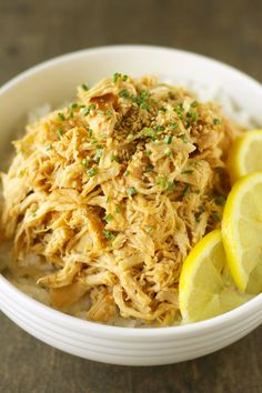 a white bowl filled with rice covered in chicken and garnished with a lemon wedge