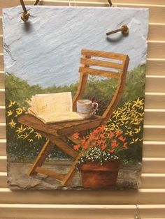 a painting of a chair with a book and cup on it hanging from a wall