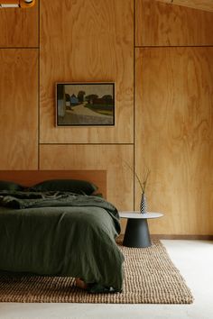 a bedroom with wood paneling and green linens on the bed, side table